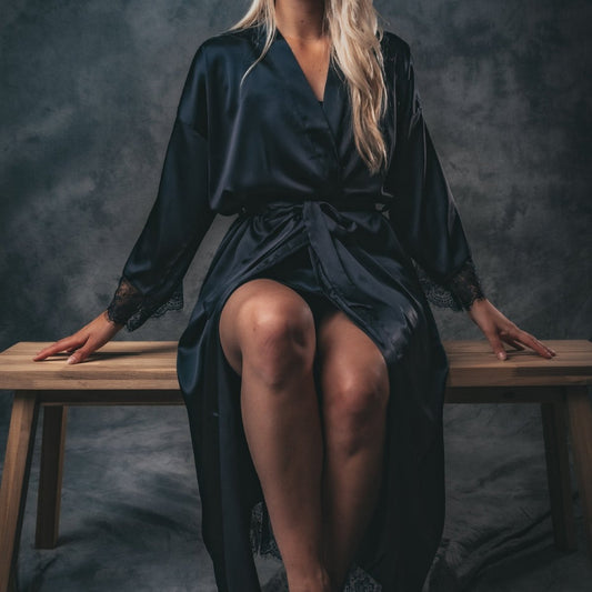 Zittend model in zwarte satijnen kimono dames met kanten details – elegante lange ochtendjas en luxe badjas satijn voor homewear en nachtkleding